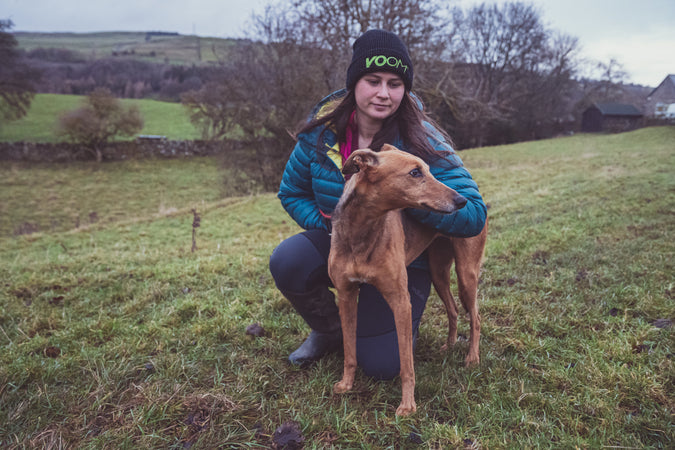 A girl bends down with her dog wearing a winter beanie by VOOM Nutrition