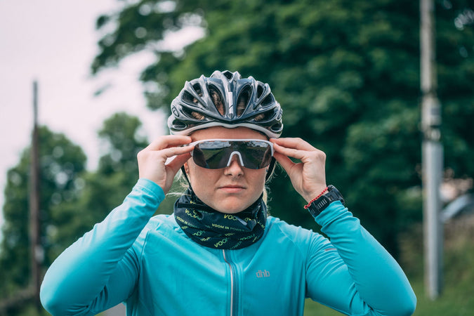 A female cyclist adjusts her glasses with the VOOM Bandana worn around her neck